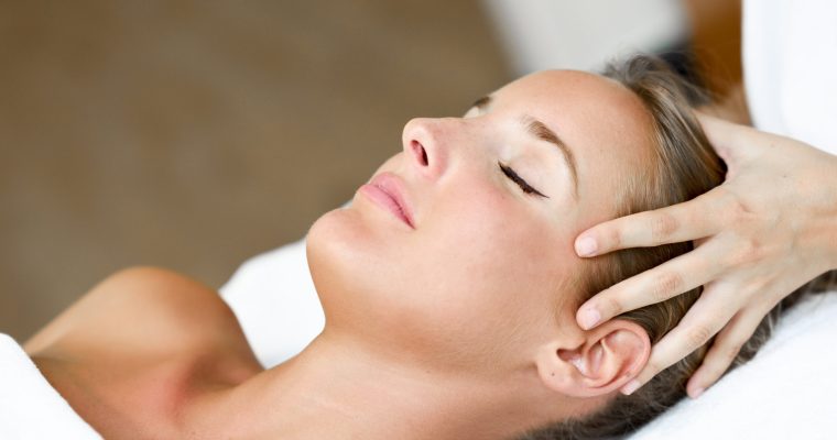 Young woman receiving a head massage in a spa center. Young blond woman receiving a head massage in a spa center with eyes closed. Female patient is receiving treatment by professional therapist.